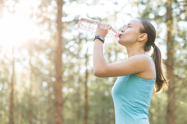 Woman drinking water after work out exercising on sunset evening