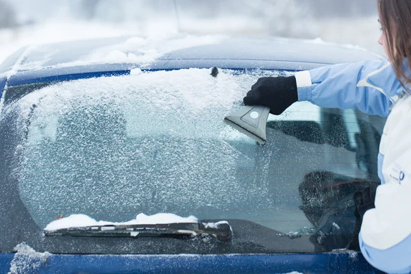 Woman clean snow from car back window with brush.
