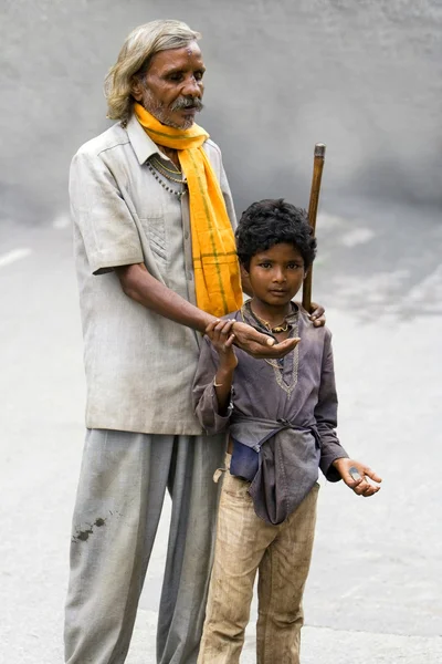 A blind man begging for money with the help of a young boy - India