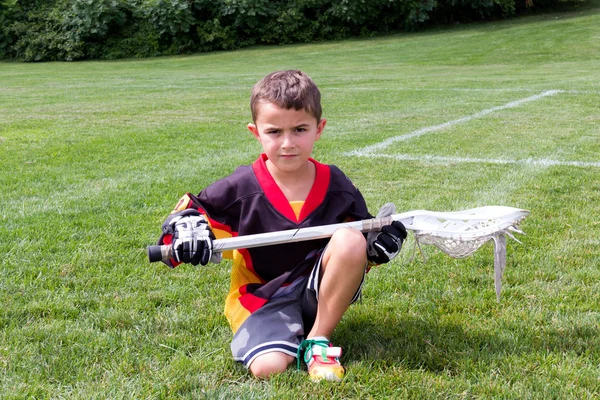 Little boy lacrosse player in the park kneeling down and posing