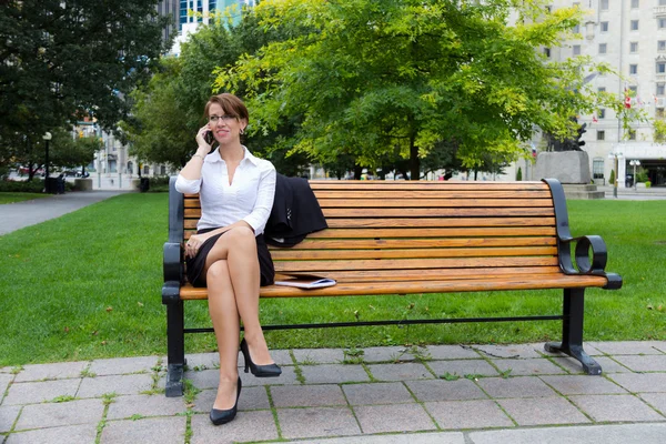 Business woman on park bench talks on phone