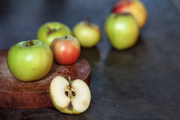 A few apples on a carving board and one half of an apple on a wooden table