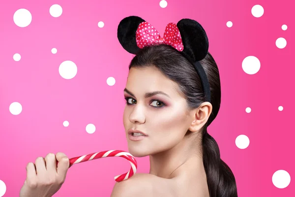 Style woman portrait perfect face, professional make. fashion mouse with big ears. Fashion art photo in bright pink background. Girl holding licorice candy.