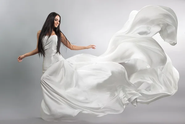 Beautiful young girl in flying white dress. Flowing fabric. Light white cloth flying in the wind