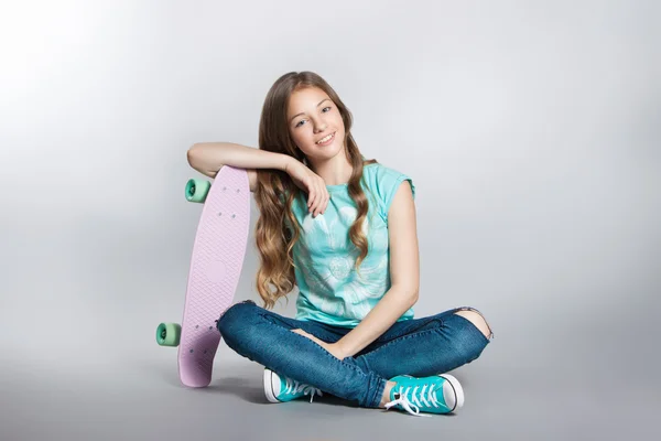 Girl posing with skateboard sitting in the studio. Joy, smile, positive emotions