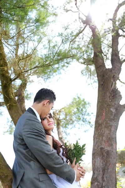 Groom embracing his bride under tree