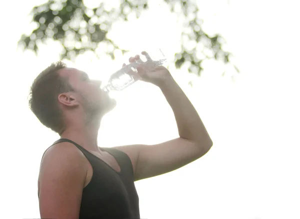 Male runner drinking mineral water at the break after running