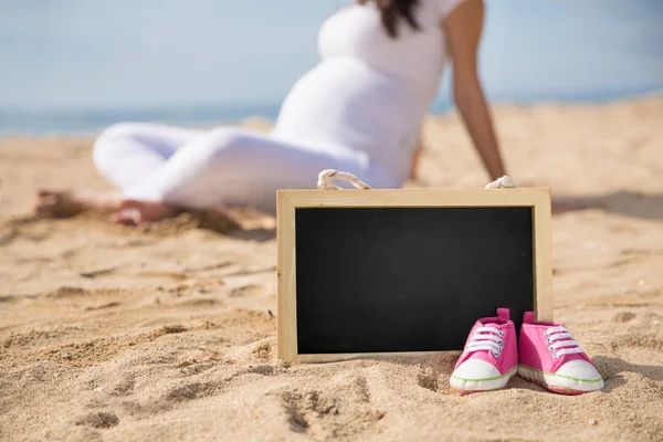 Pink Toddler sneakers and mini chalk board on the sand with preg