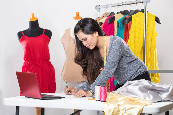 Young asian designer woman using a laptop and smiling,clothes ha