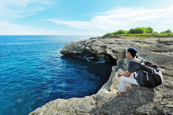 An explorer sitting on the edge of a cliff overlooking the blue