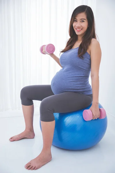 Asian pregnant woman doing exercise with swiss ball, smiling