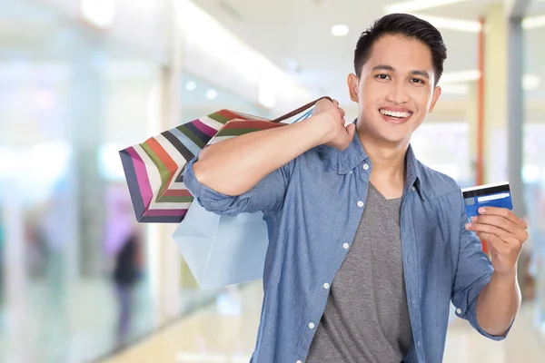 Young asian man holding shopping bags and credit card, close up