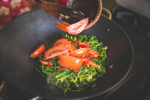 Adding red sliced tomato into water spinach stir-fry, close up
