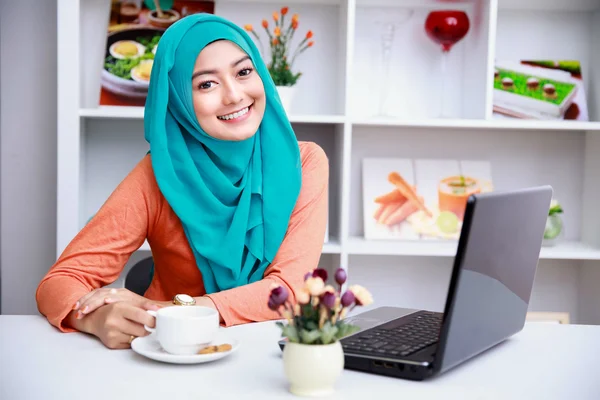 Attractive young muslim woman enjoying a cup of tea while using