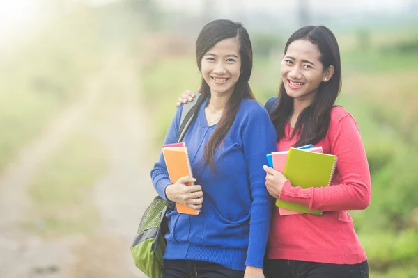 Two young Asian students holding books, smiling brightly to the