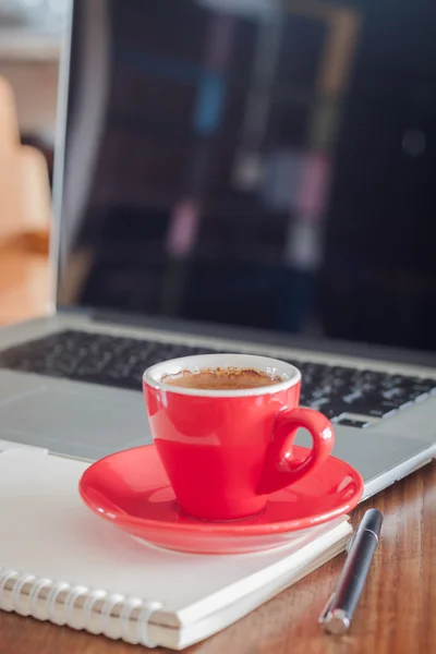 Red coffee cup with notepad and laptop