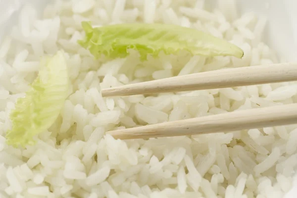 White plate of cooked long-grain rice on wooden background. Healthy eating, diet, vegetarianism.