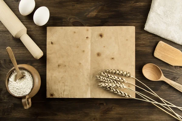 Open old vintage book on the aged wooden background. Kitchen utensils, ears of wheat, flour in a pot. homemade, menu, recipe, mock up