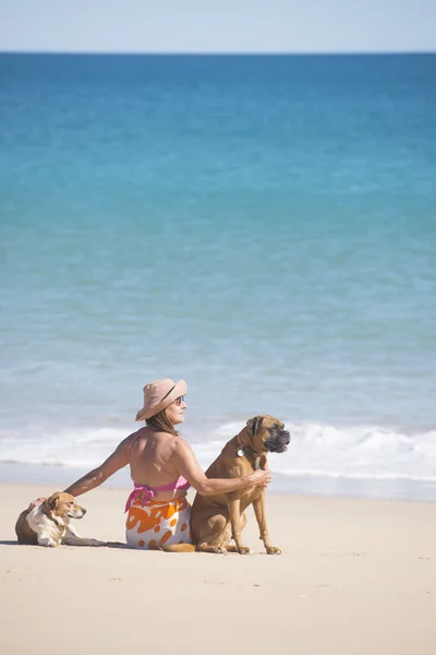 Mature Woman and pet dogs sitting at tropical beach