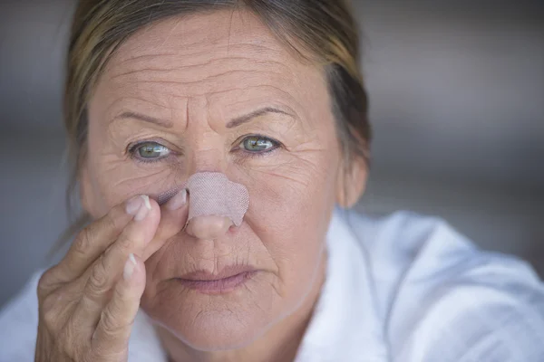 Unhappy woman with band aid on injured nose