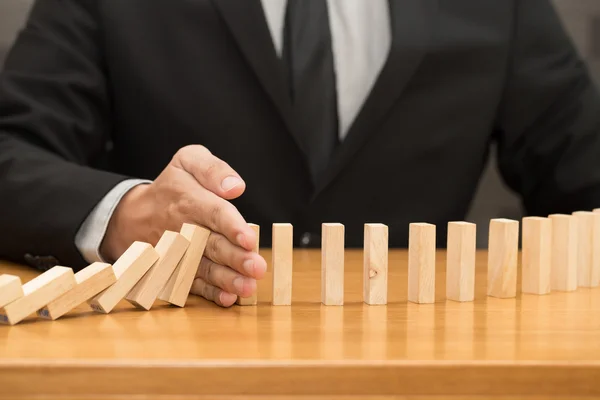 Hand of businessman stopping the domino effect. Risk control con