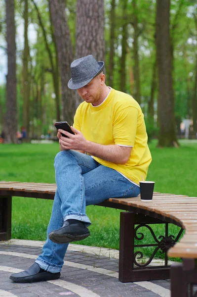 Man sits on bench in park with smartphone