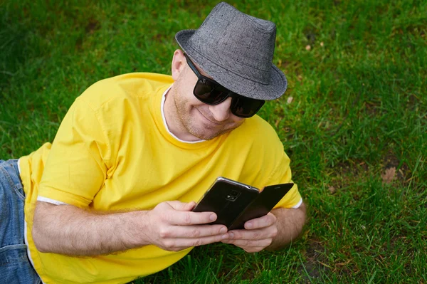 Smart young man in a yellow T-shirt with the phone on the grass
