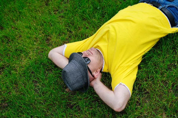 Man in a yellow T-shirt and hat lying on the grass