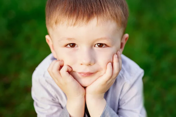 Boy sits on the green grass in the summer park close up