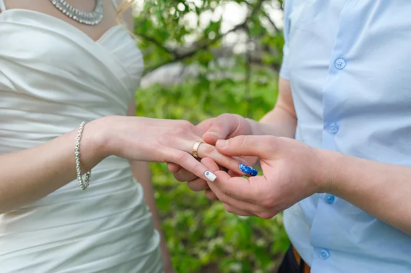 Groom wears bride a gold ring on his finger in the garden