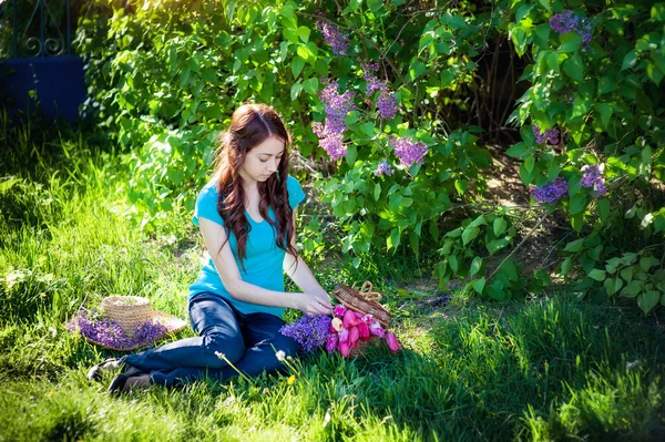 Beautiful girl sitting on the grass with a bouquet of lilac in spring park