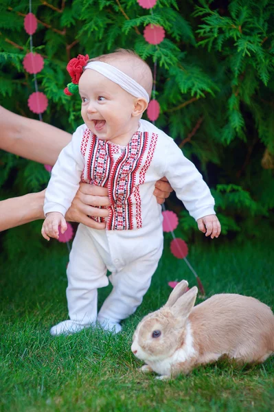 Cute funny happy baby with rabbit making his first steps on a green grass