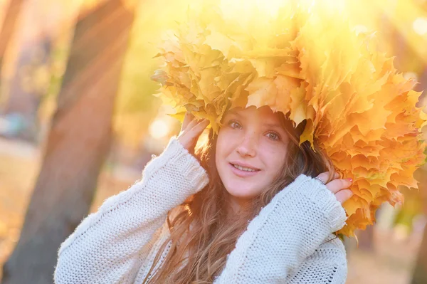 Happy young woman with a wreath of yellow leaves walking in the park
