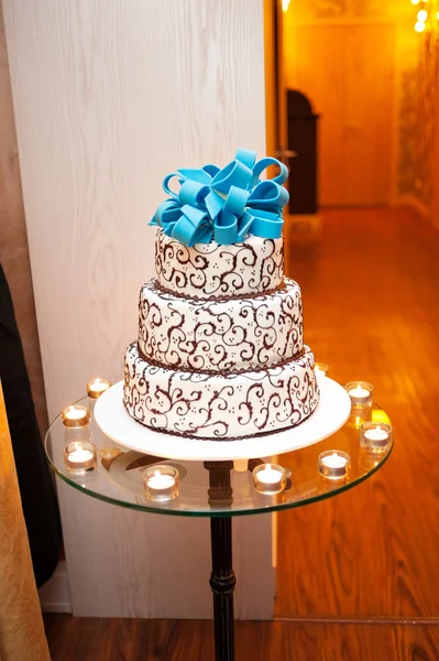Beautiful white three-tier cake with a turquoise bow on top is on the table