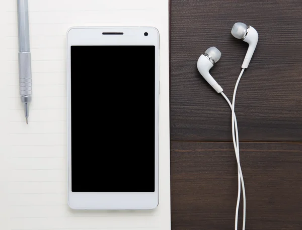 White smartphone with headphones on the old wooden board