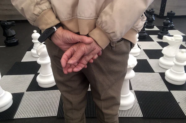 Hands of an 0ld man play giant street chess