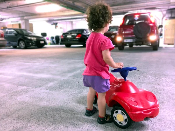 Little girl play with a toy car in parking lot