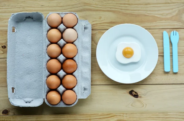 Flat lay of eggs tray beside a white plate with sunny side up eg