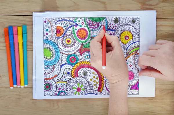 Woman hands coloring  patterns on a coloring page for stress rel