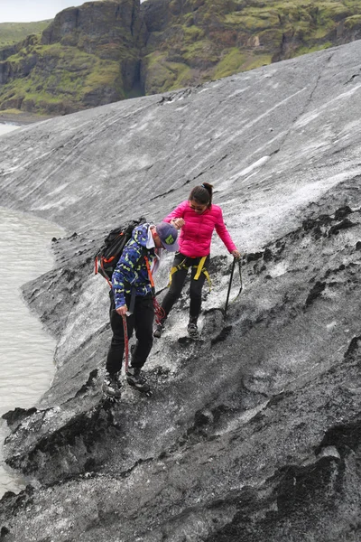 Tour guide helping tourist during glacier walk at Solheimajokull glacier
