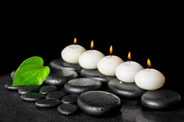 Spa still life of row white candles and green leaf on black zen
