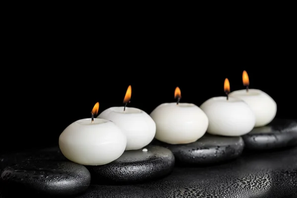 Spa concept of white candles on zen stones with water dew black