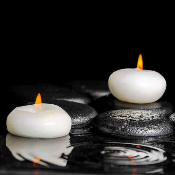 Beautiful spa concept of white candles and black zen stones on r