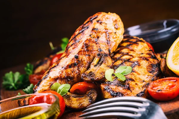 Grilled chicken breast in different variations with cherry tomatoes,  mushrooms, herbs, cut lemon on a wooden board or teflon pan. Traditional cuisine. Grill kitchen