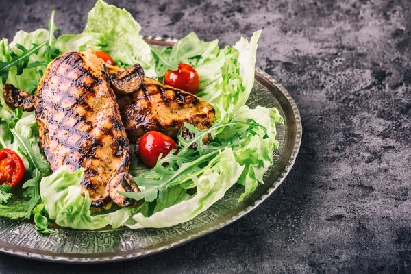 Grilled chicken breast in different variations with lettuce salad cherry tomatoes  mushrooms herbs cut lemon on a wooden board or teflon pan. Traditional cuisine. Grill kitchen