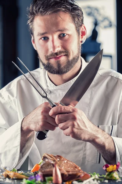 Chef. Chef funny. Chef with knife and fork arms crossed. Professional chef in a restaurant or hotel prepares or cut up T-bone steak. Chef preparing steak. Cook for their work on catering