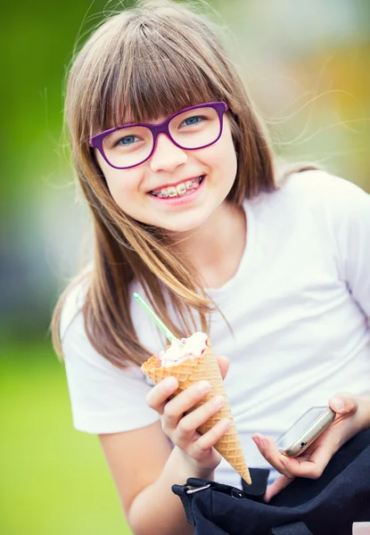 Cute little girl in the park on a sunny day with ice cream and mobile phone