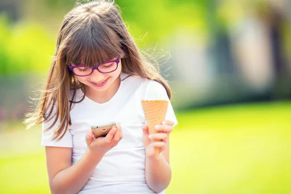 Cute little girl in the park on a sunny day with ice cream and mobile phone