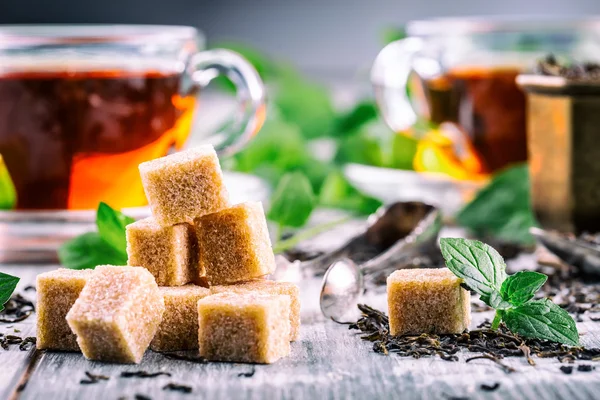 Sugar. Cane sugar. Cane sugar cubes heap close up macro shot. Tea in a glass cup, mint leaves, dried tea, sliced lime, cane brown sugar