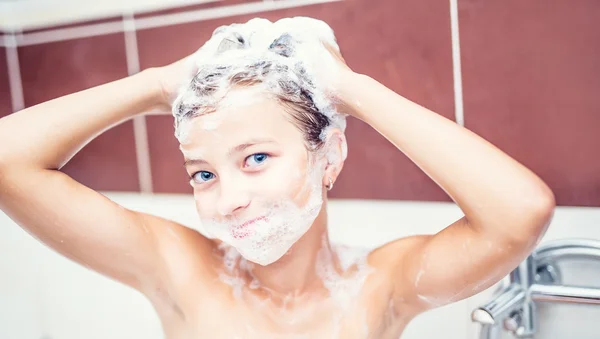 Cute young girl in shower washing hair and face with shampoo. girl with braces